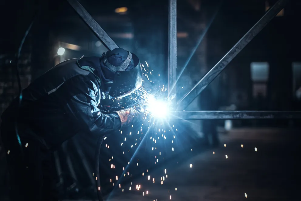 Homem com equipamento de solda realizando a solda e faíscas saindo